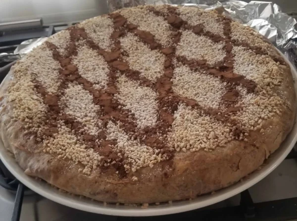 A golden, crispy Moroccan Chicken Pastilla dusted with powdered sugar and cinnamon on a serving plate.