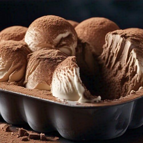 Overhead shot of creamy Tiramisu Ice Cream in a pan with cocoa powder dusting and a scoop removed.1